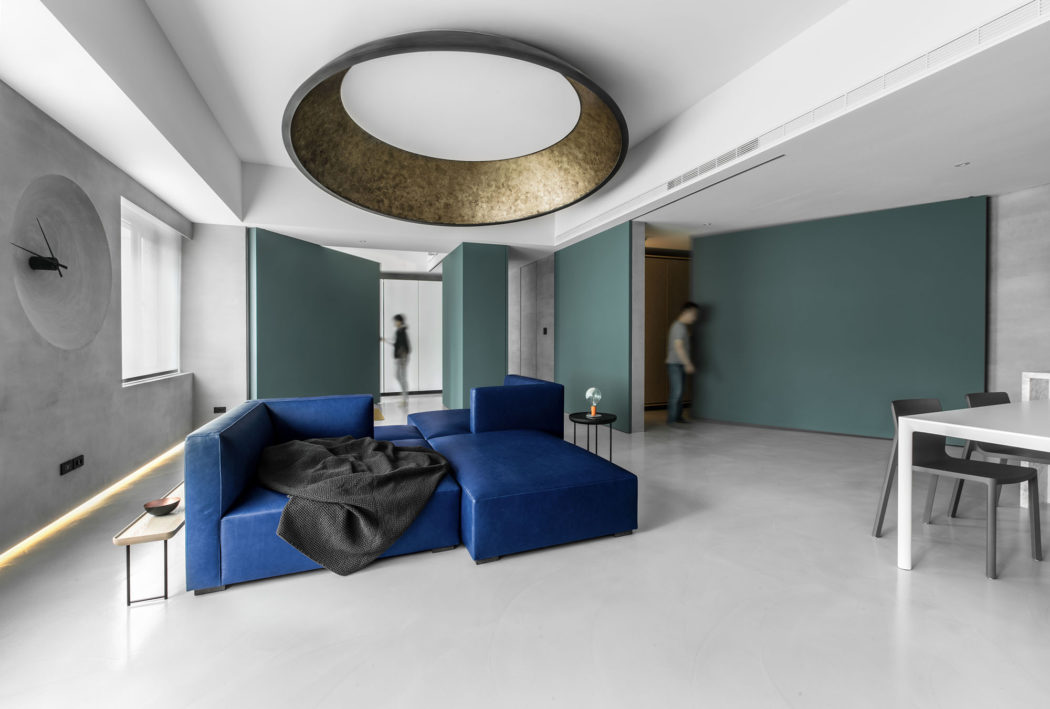 Minimalist living room with sleek blue sofa, gold circular ceiling light, and green accent walls.