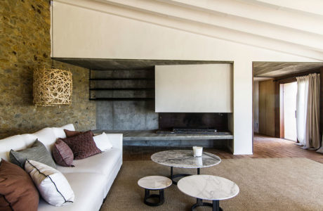 Rustic stone walls, sleek concrete fireplace, and minimalist marble coffee tables.