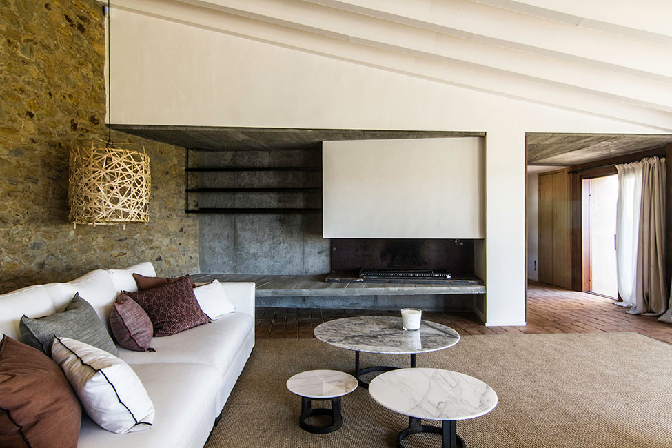 Rustic stone walls, sleek concrete fireplace, and minimalist marble coffee tables.