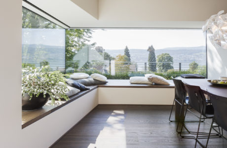 A modern, open-concept living space with panoramic windows overlooking lush greenery.