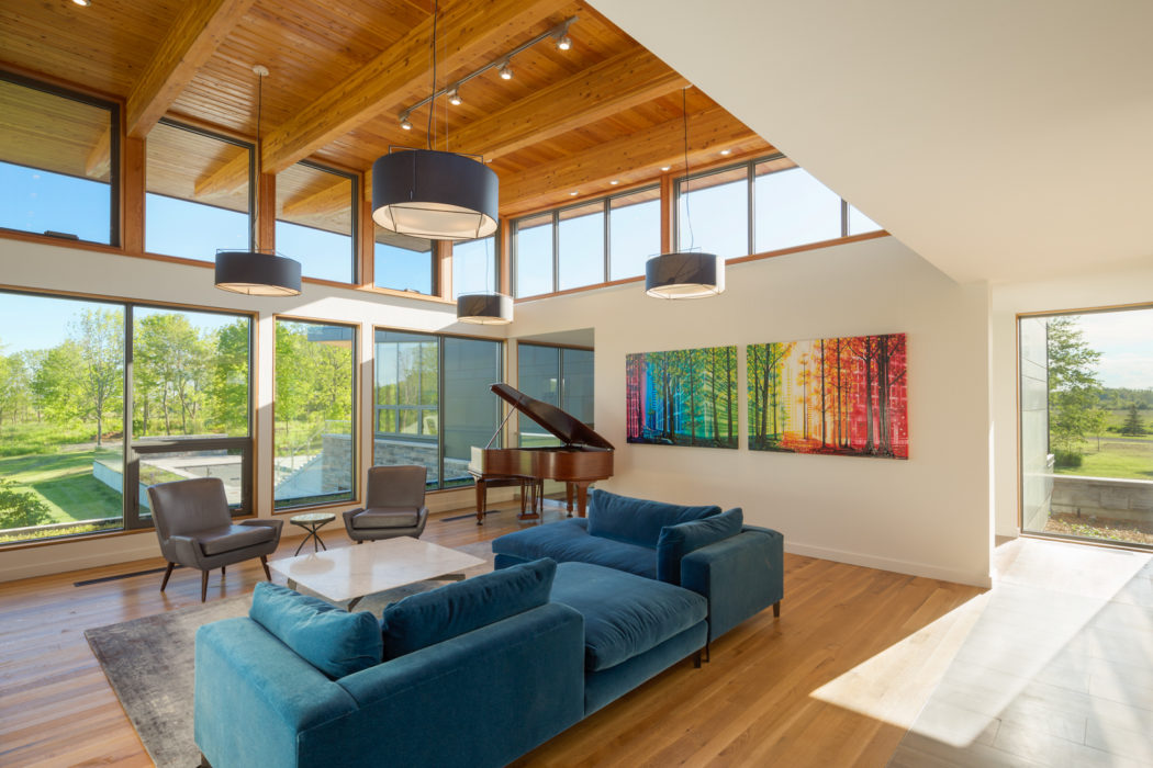 Spacious open-concept living room with wall-to-wall windows, wooden beams, and colorful artwork.