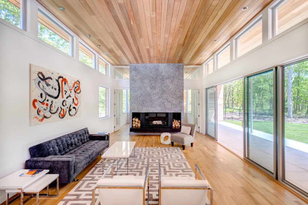 Modern living room with wooden ceiling, large windows, and central fireplace.