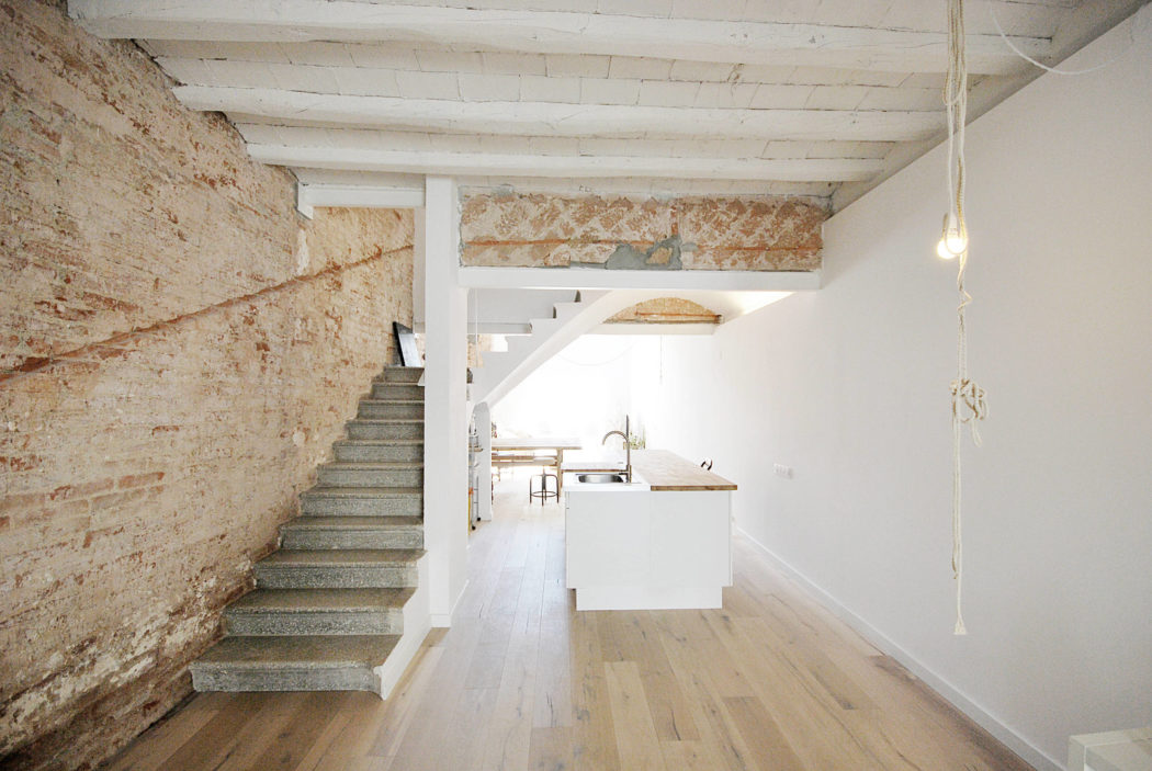Rustic interior with exposed stonework, wooden beams, and a minimalist staircase.