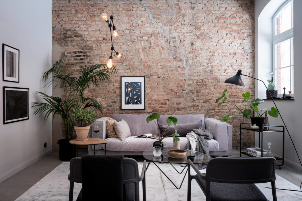 A cozy living room with exposed brick walls, modern furnishings, and lush houseplants.