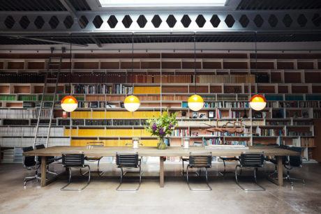 Modern open-plan dining room with wooden shelves, colorful lighting, and a large central table.