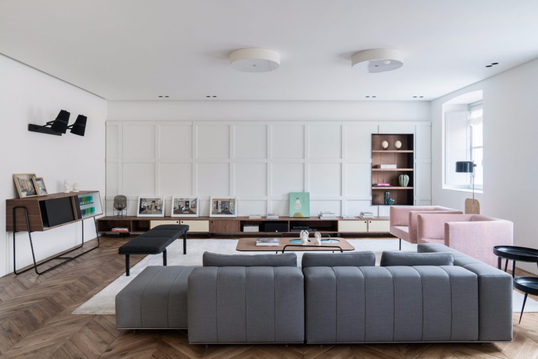 Contemporary living room with minimal white walls, gray modular sofa, and wooden shelving.