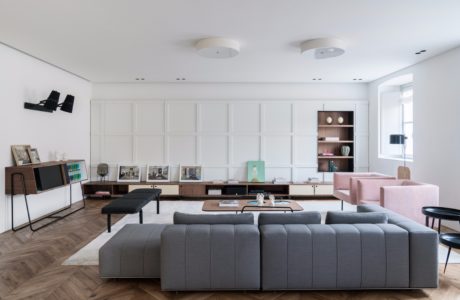 Contemporary living room with minimal white walls, gray modular sofa, and wooden shelving.