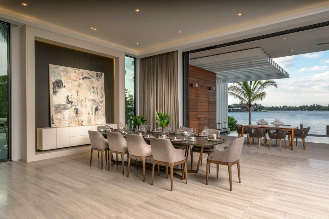 Sleek, modern dining room with large windows overlooking a scenic lake and palm tree.