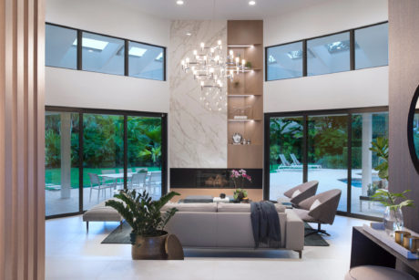 Spacious modern living room with large windows, marble fireplace, and lush tropical view.