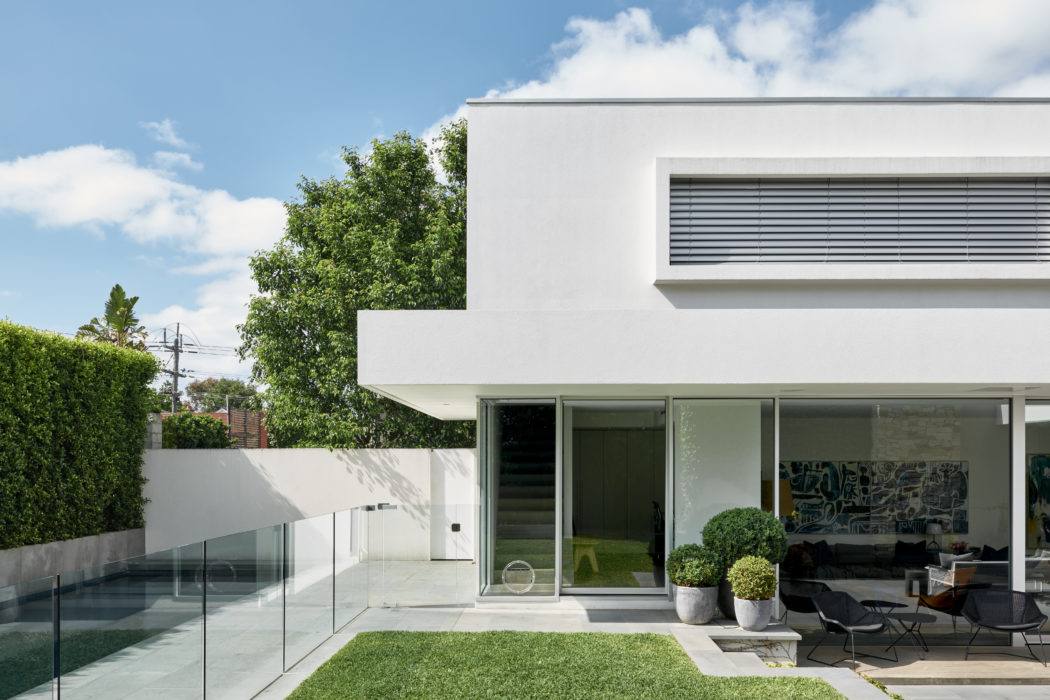 A sleek, modern home with a lush green lawn, glass walls, and a stylized, minimalist exterior.