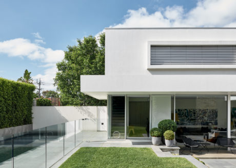 A sleek, modern home with a lush green lawn, glass walls, and a stylized, minimalist exterior.