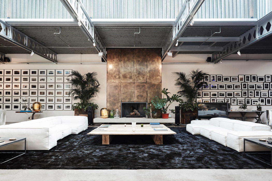 Spacious industrial-style loft with large fireplace, potted plants, and expansive sofa seating.