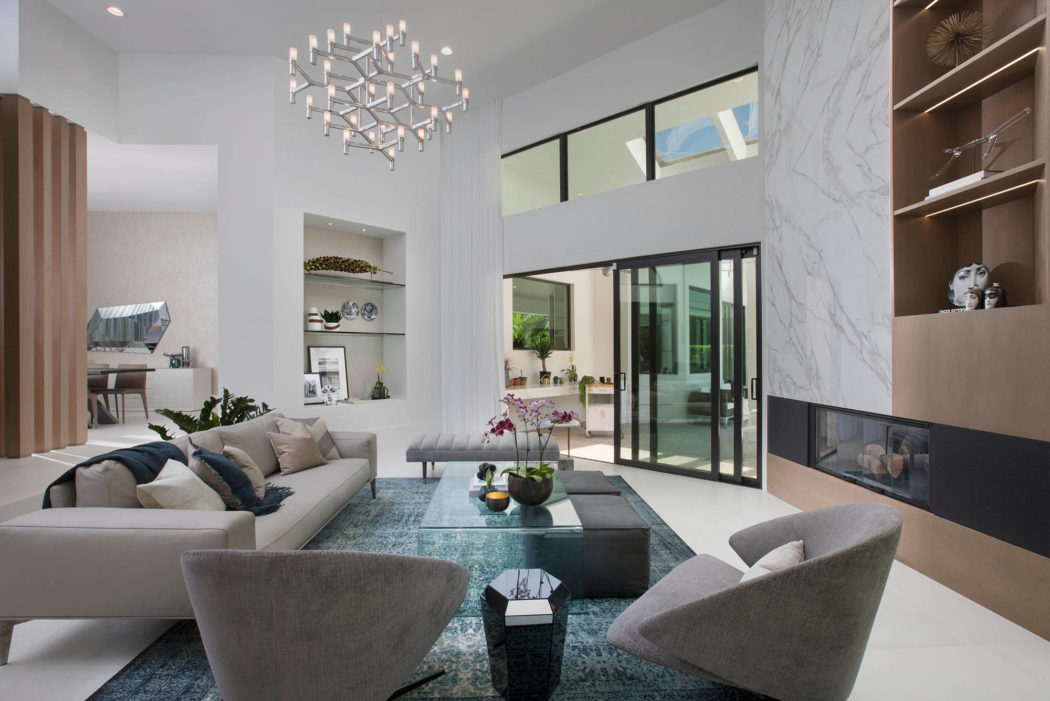 Spacious modern living room with sleek furniture, marble walls, and a dramatic chandelier.