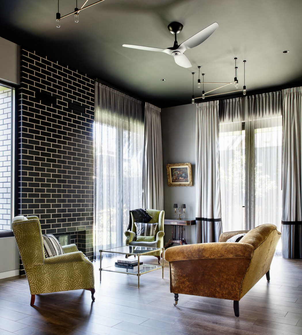 A cozy living room with a black brick wall, plush leather and velvet armchairs, and sleek modern lighting.