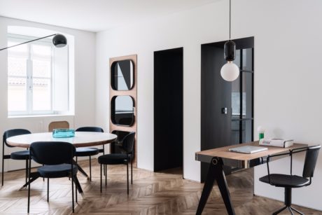 Modern, minimalist dining and office space with wooden floors, black accents, and large windows.
