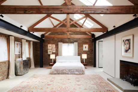 A spacious bedroom with exposed wooden beams, brick walls, and warm lighting.
