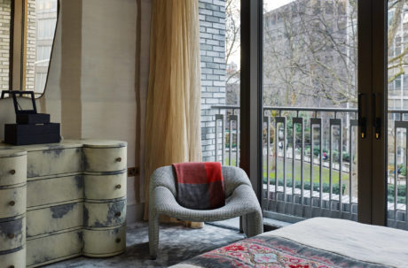 Chic bedroom with houndstooth chair and distinctive dresser by window.