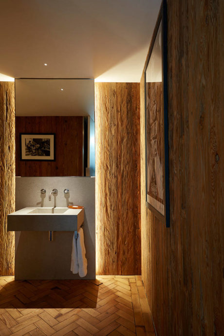 A cozy bathroom with wooden paneled walls, a modern sink, and a herringbone tile floor.