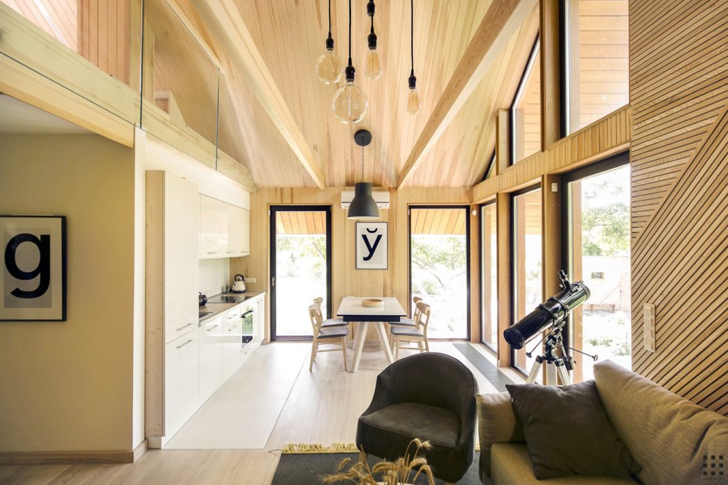 An open-concept, modern cabin-style interior with a vaulted wood-paneled ceiling, minimalist decor, and large windows providing natural light.