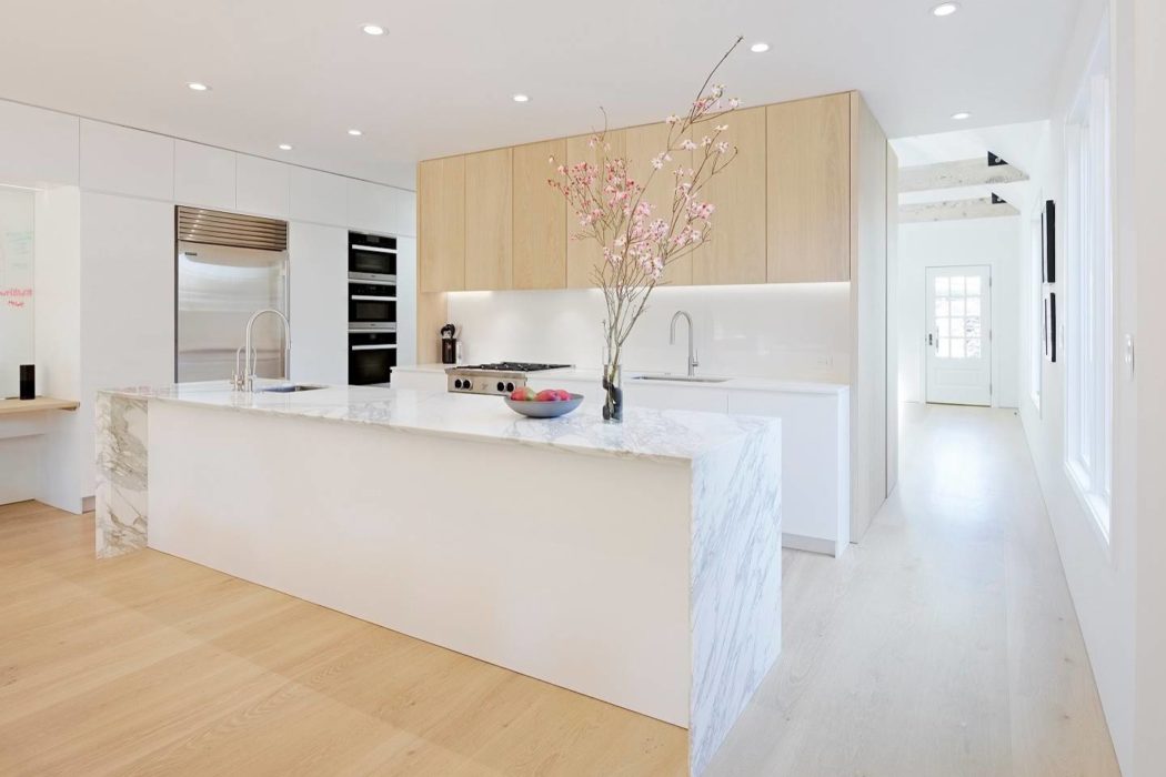 Bright minimalist kitchen with marble island and light wood cabinets.
