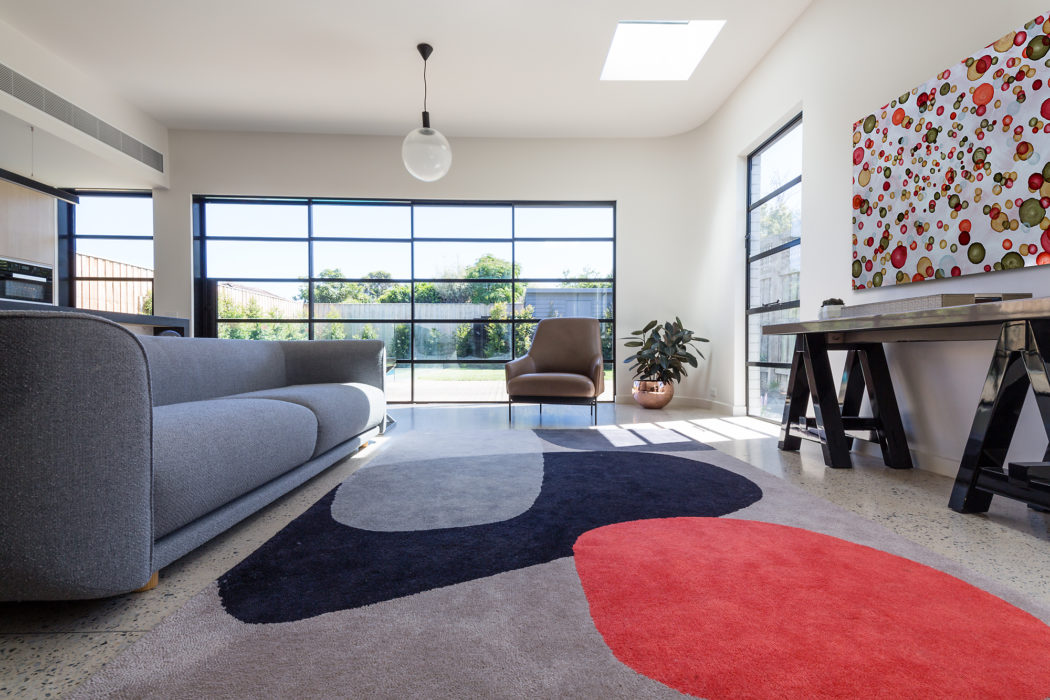 Modern living room with large windows, colorful rug, and pendant light.