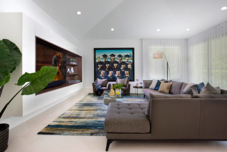 A modern and spacious living room with sleek furniture, a large wall-mounted TV, and a colorful area rug.