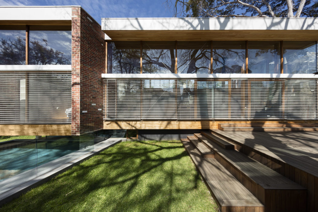 Brick exterior, wood deck, glass walls, and large windows showcasing modern architecture.