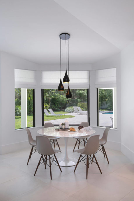 Elegant dining area with minimalist furnishings and floor-to-ceiling windows overlooking a lush outdoor garden.