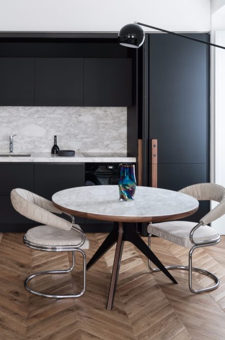 Modern kitchen with elegant marble countertop, wooden floors, and angular chairs.