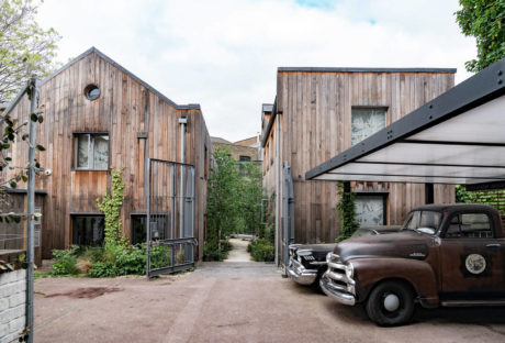 Rustic wooden buildings, vintage car, and green foliage create a charming industrial-style setting.