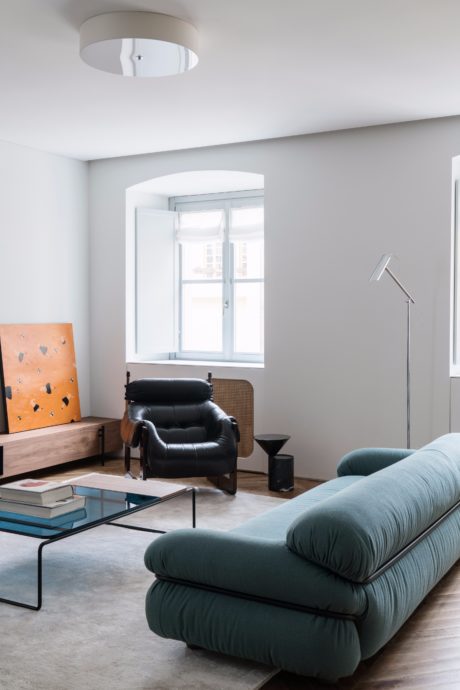 A modern, minimalist living room with a black leather armchair, a blue sofa, and a glass coffee table.