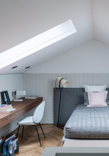 Minimalist bedroom design with wood desk, gray headboard, and recessed ceiling light.