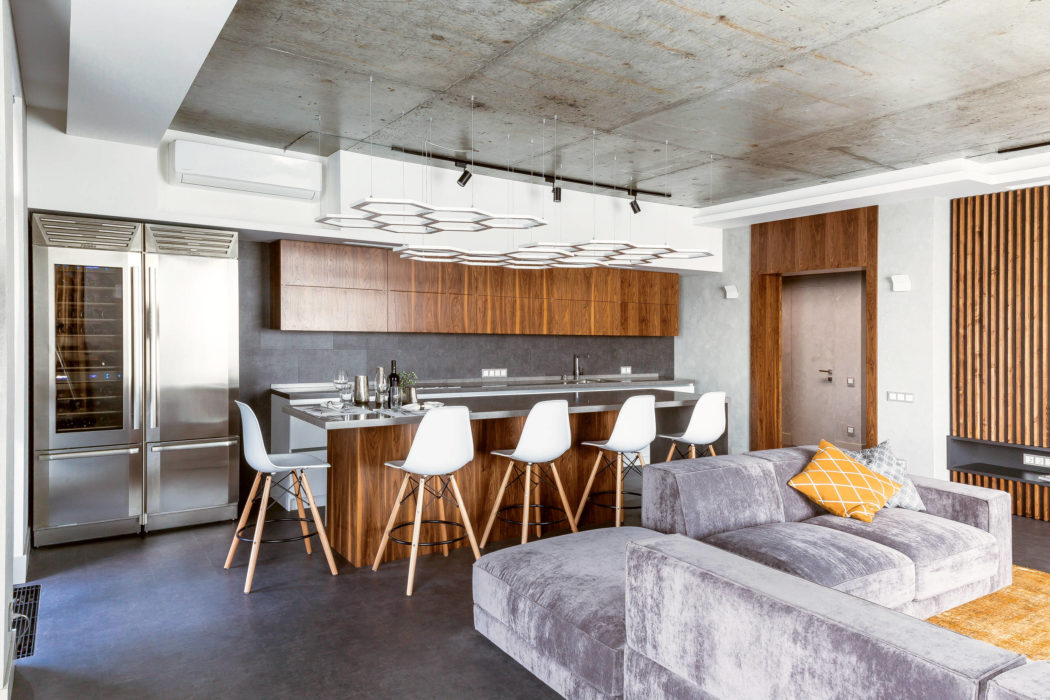 Modern kitchen and living room with minimalist furniture, concrete ceiling, and warm wood cabinetry.
