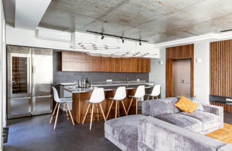 Modern kitchen and living room with minimalist furniture, concrete ceiling, and warm wood cabinetry.