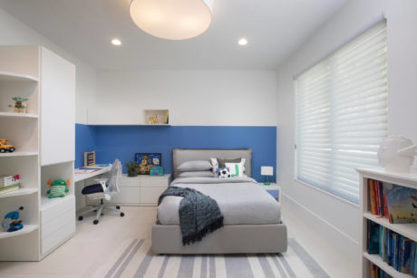 A modern, well-designed child's bedroom with blue accent wall, white furniture, and ample storage.