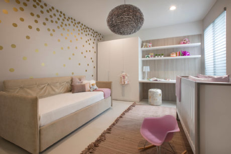 A modern nursery with gold polka dot wall decor, beige couch, and white shelving unit.