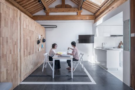 Rustic wooden interior with high ceiling, modern kitchen and two people at table.