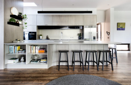 Modern, open-concept kitchen with sleek gray cabinetry, floating shelves, and bar seating.