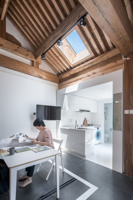 Cozy wooden ceiling, modern kitchen, and a person working at a white desk in a bright space.