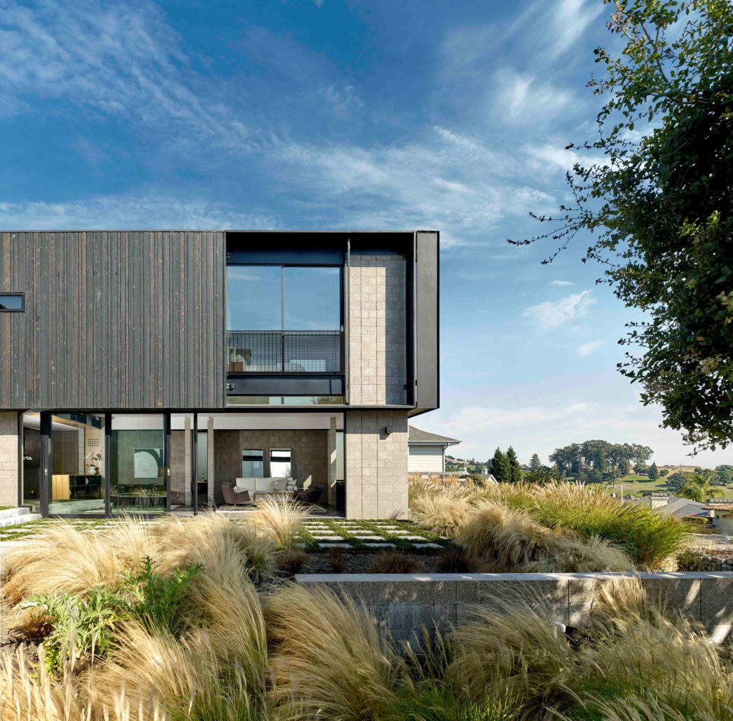 Modern, asymmetric facade with glass walls and wooden siding, surrounded by lush landscaping.