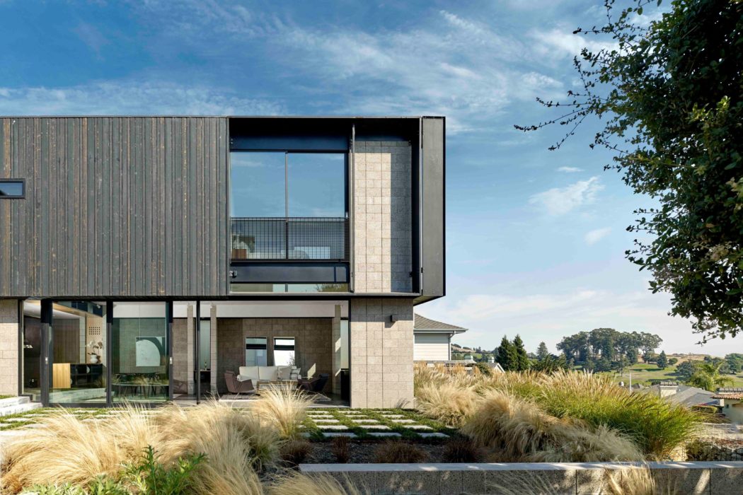 Modern, asymmetric facade with glass walls and wooden siding, surrounded by lush landscaping.