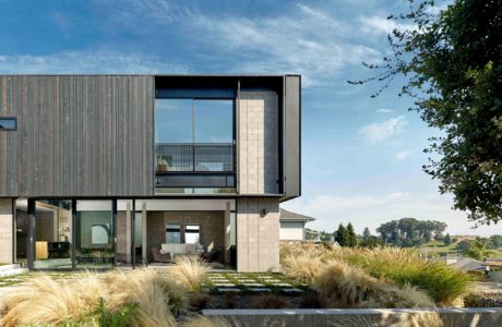 Modern, asymmetric facade with glass walls and wooden siding, surrounded by lush landscaping.