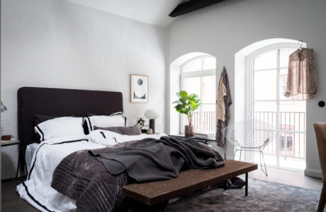 A spacious, modern bedroom with large arched windows, an elegant black bed, and a mix of textures.