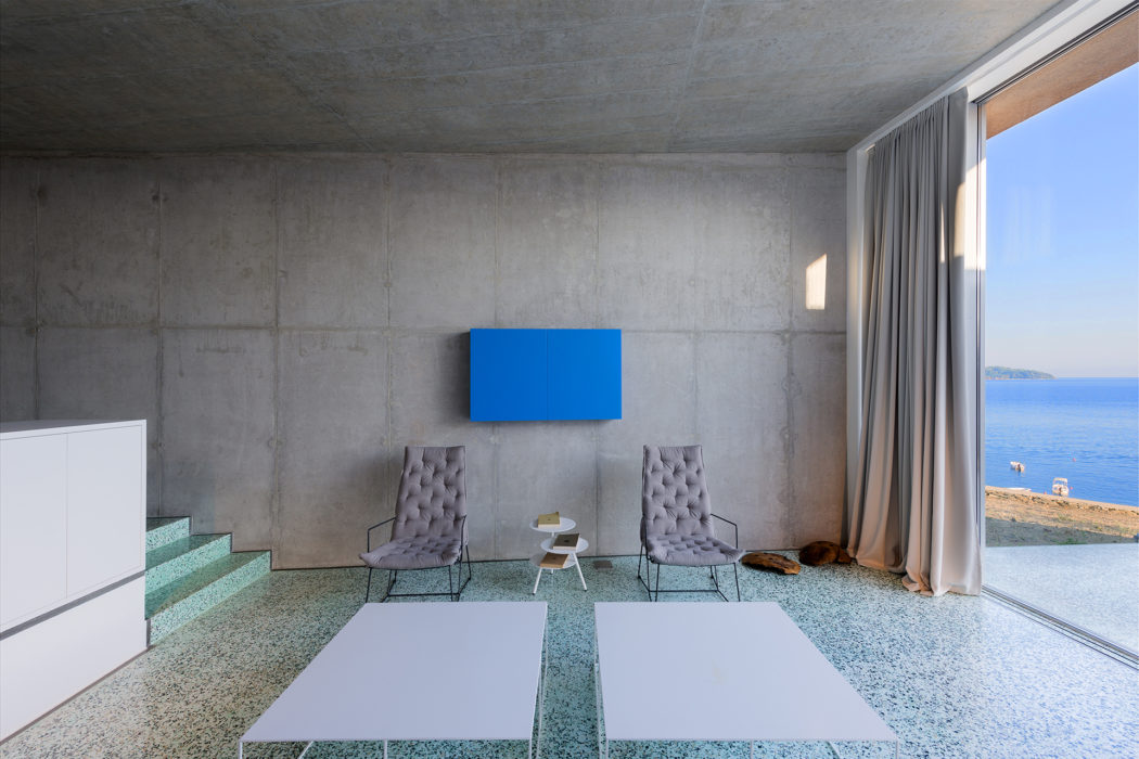 Minimalist interior with concrete walls, blue artwork, overlooking the sea.