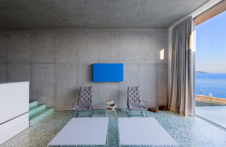 Minimalist interior with concrete walls, blue artwork, overlooking the sea.