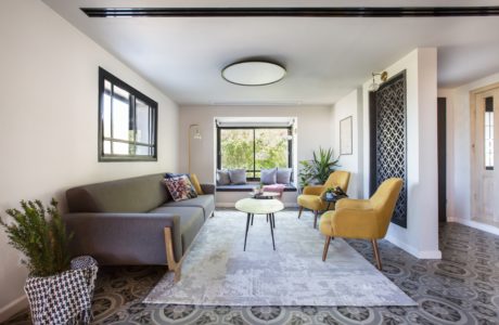 Modern living room with gray sofa, yellow armchairs, patterned rug,