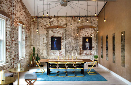 Modern dining room with exposed brick walls, long table, blue chairs, and unique