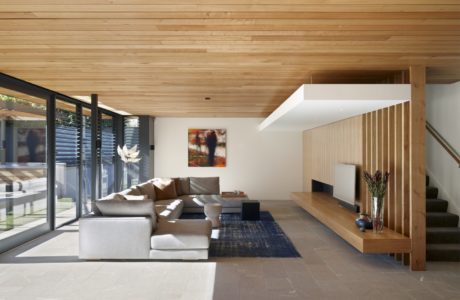 Modern living room with wooden ceiling, stairs, and large windows.