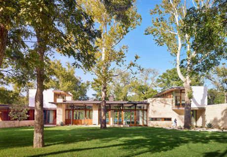 Modern house with large windows nestled among green trees.