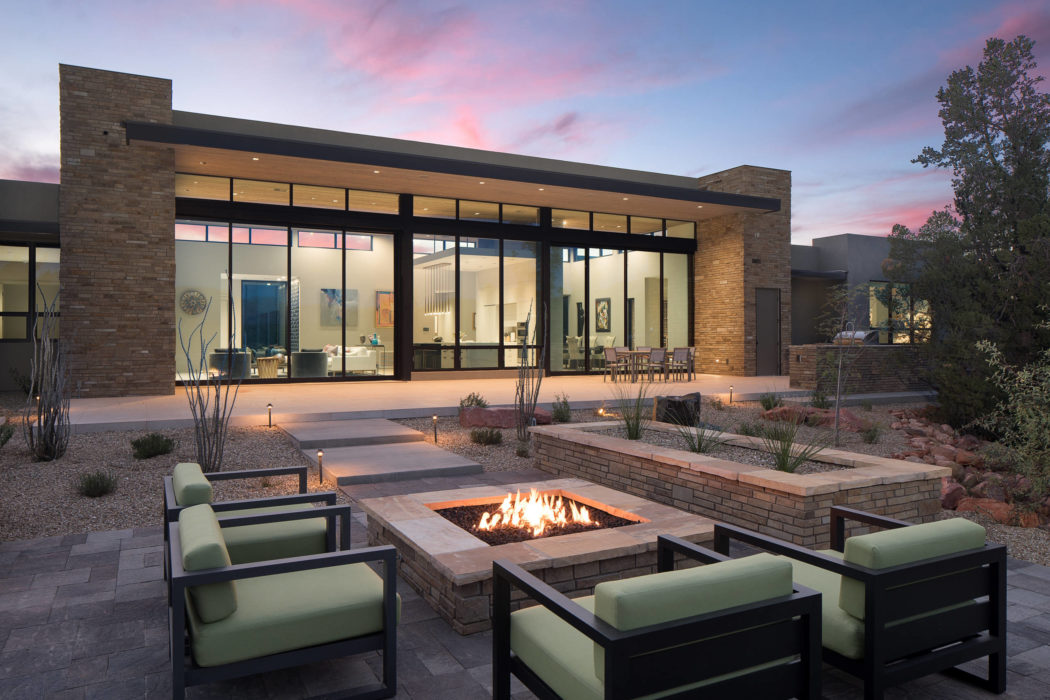 Modern house with large windows and outdoor fire pit at twilight.